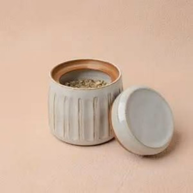 This small lidded jar in Linen glaze has a quiet, understated beauty. The glaze settles into a soft, pale gray with a slightly warm undertone, and where it thins over the carved vertical lines that encircle the body, the warm, sandy brown clay peeks